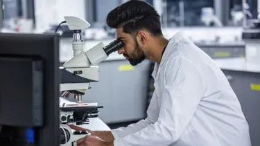 A male biomedical scientist working in a lab, looking through a microscope
