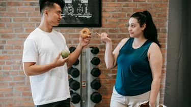 Two people in a gym deciding if they should eat a donut.