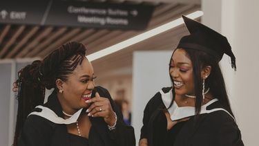 Two female graduates in graduation gowns congratulating each other.